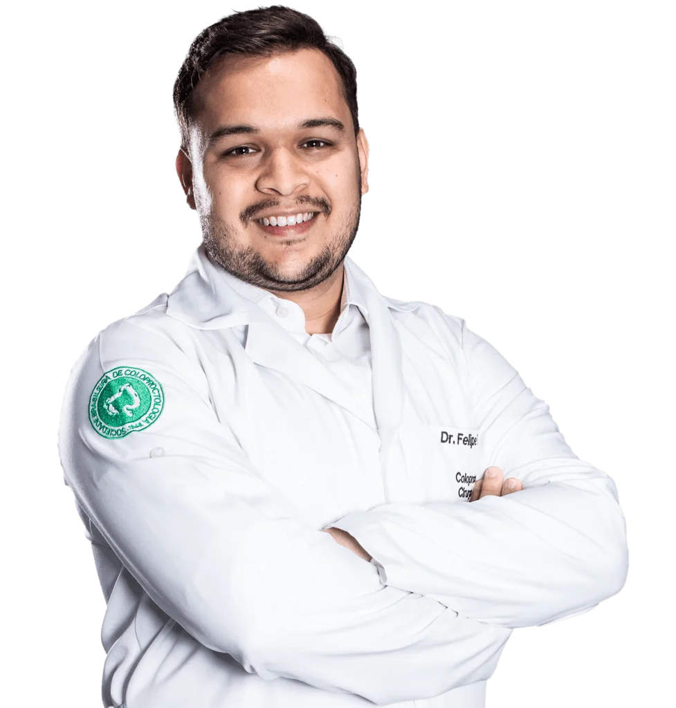 Dr. Felipe Pereira Gomes sorrindo, de jaleco branco com o brasão da Sociedade Brasileira de Coloproctologia no ombro
